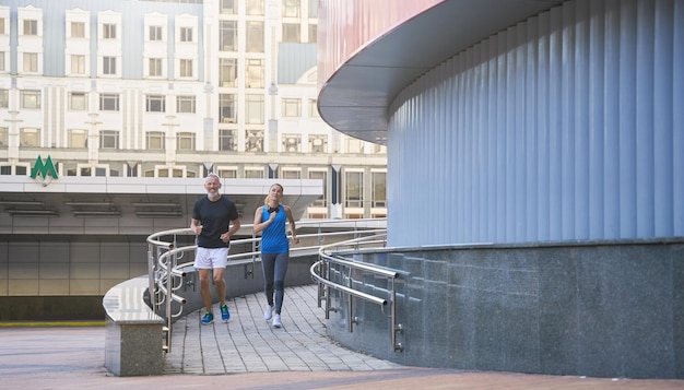 Aktives Paar mittleren Alters in Sportkleidung, das morgens zusammen in der Stadt läuft