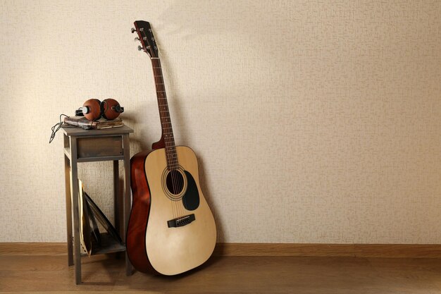 Akustikgitarre an der Wand mit Hocker und Kopfhörern im Raum