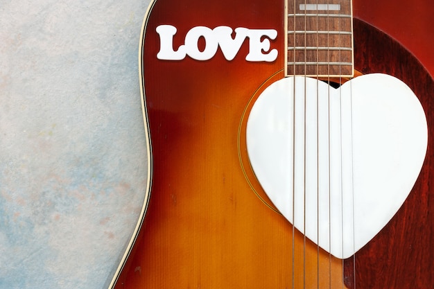 Akustikgitarre, hölzernes weißes Herzformsymbol und Wort LIEBE auf himmelblauem Hintergrund. Ansicht von oben, Nahaufnahme, Kopienraum.