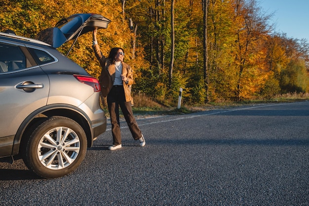 al atardecer una mujer sonriente cierra el maletero de un coche estacionado