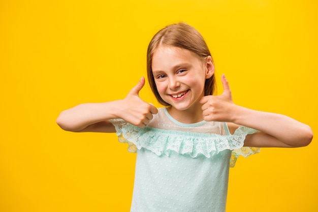 Foto al igual que y aprobación retrato de estudio de niños pequeños con estilo niña gestando pulgares hacia arriba y mirando a