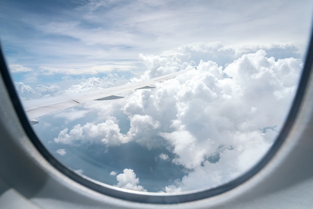 Ala del aeroplano que vuela sobre las nubes en el fondo del cielo azul a través de la ventana.