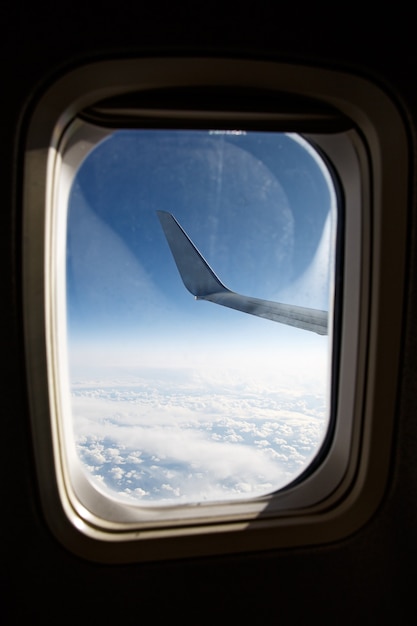 Ala de un avión sobre las nubes azules en el ojo de buey.