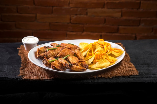 Ala de pollo con tortillas de patata sobre tela marrón y madera negra sobre fondo de ladrillos