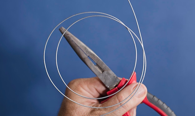 Foto alambre en espiral grueso con pinzas de sujeción y corte fondo azul