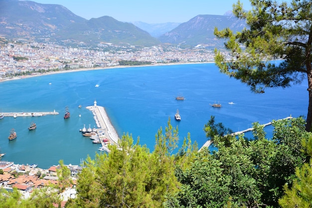 Alanya-Seehafen mit Leuchtturm und Uferpromenade, Blick vom Gipfel des Berges durch Pinien