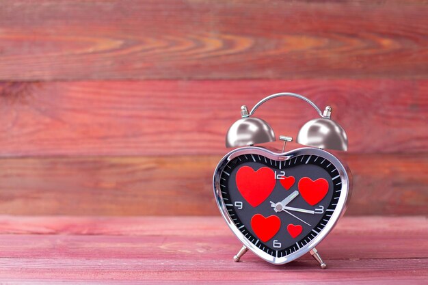 Alarma de reloj de acero en forma de corazón con corazones rojos sobre un fondo de madera rosa Día de San Valentín