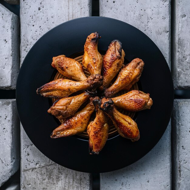 Foto alas de pollo asadas en un plato negro con salsa de barbacoa directamente por encima