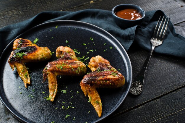 Las alas de pollo asaron a la parrilla en adobo de la miel en una placa negra.