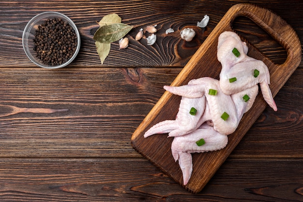 Alas de pollo crudo en mesa de madera oscura.