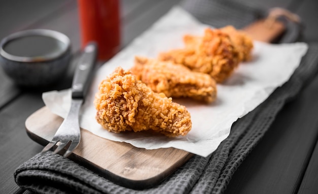 Alas de pollo frito de alto ángulo en la tabla de cortar con un tenedor