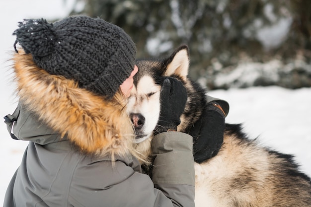 Alaskan malamute besándose con mujer en bosque de invierno