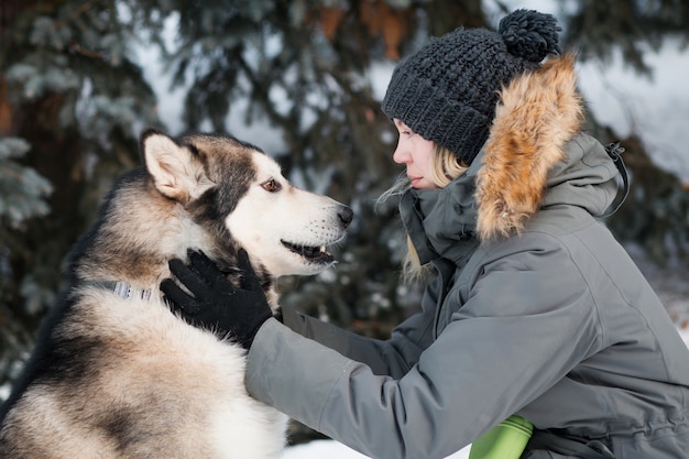 Alaskan Malamute, der einander mit Frau im Winterwald ansieht