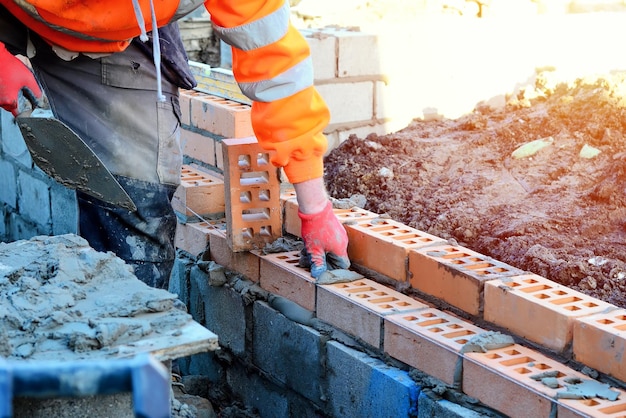 Albañil industrial poniendo ladrillos en la mezcla de cemento en el sitio de construcción Lucha contra la crisis de la vivienda