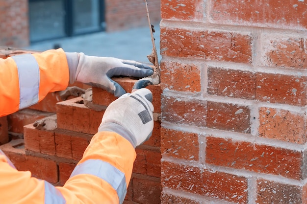 Albañil poniendo ladrillos sobre mortero en la construcción de viviendas residenciales Obtener calificación de construcción