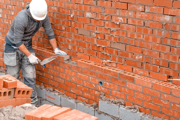 Foto albañil poniendo ladrillos sobre mortero en la nueva construcción de viviendas residenciales