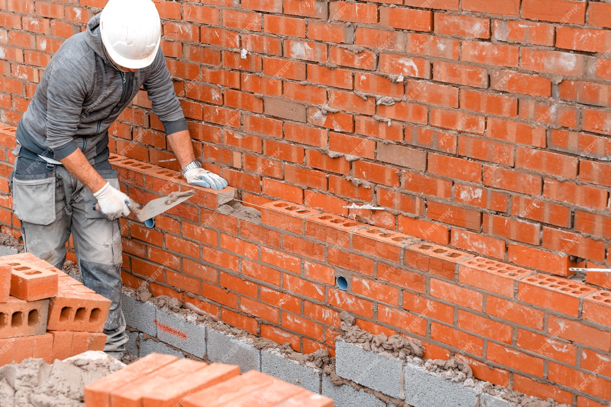 Albañil poniendo ladrillos sobre mortero en la nueva construcción de viviendas residenciales | Foto Premium