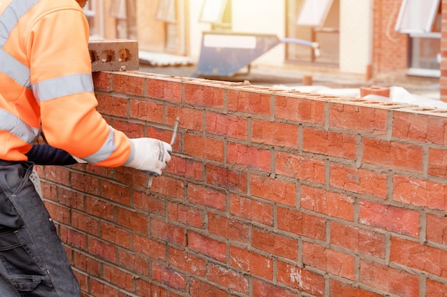 Albañil poniendo ladrillos sobre mortero en la nueva construcción de viviendas residenciales