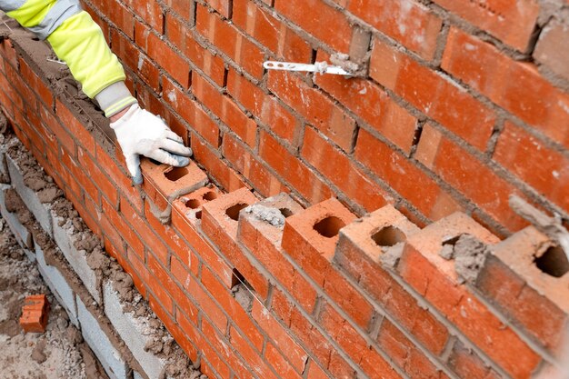 Albañil poniendo ladrillos sobre mortero en la nueva construcción de viviendas residenciales