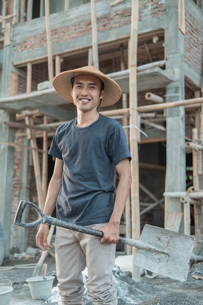 Albañil con un sombrero sonriente se levanta con una pala en la construcción inconclusa de la casa