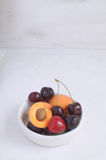 Albaricoques y cerezas en un tazón de porcelana blanca Frutas y bayas de verano Cosecha de frutas orgánicas