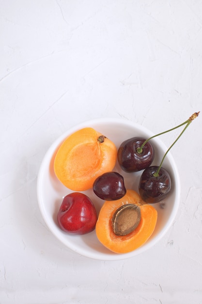 Albaricoques y cerezas en un tazón de porcelana blanca Frutas y bayas de verano Cosecha de frutas orgánicas