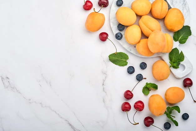 Albaricoques frescos, cereza roja y mora sobre fondo de mármol blanco. Vegetariano, pérdida de peso, concepto de alimentación limpia y saludable. Vista superior. Copie el espacio.