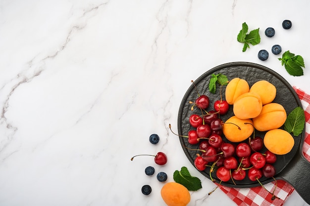 Albaricoques frescos, cereza roja y mora sobre fondo de mármol blanco. Vegetariano, pérdida de peso, concepto de alimentación limpia y saludable. Vista superior. Copie el espacio.