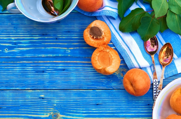 Albaricoques naranjas frescos sobre un fondo de madera azul y medio con una piedra. servilleta, cucharas y hojas verdes.