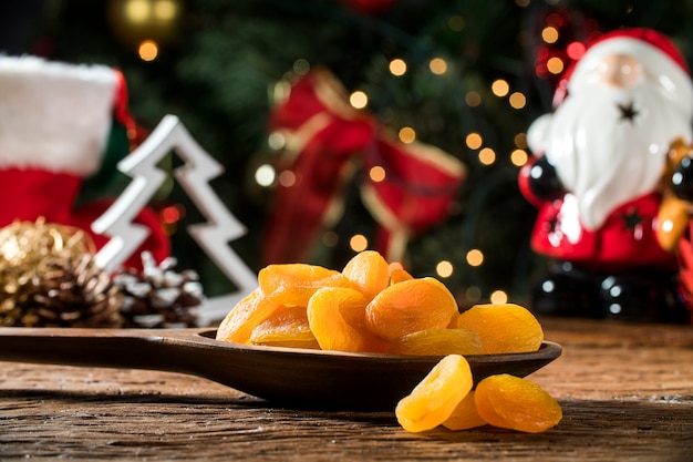 Albaricoques secos en un recipiente en el tablero con fondo borroso de Navidad