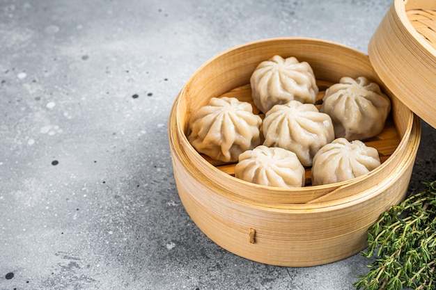 Albóndigas de baozi al vapor rellenas de carne en una vaporera de bambú. fondo gris. Vista superior. Copie el espacio.