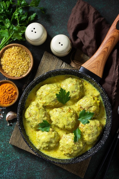 Albóndigas con bulgur en crema agria y salsa de cúrcuma en una sartén sobre una encimera de piedra oscura Vista superior