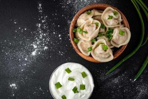 Albóndigas de carne en un tazón de madera con crema agria y cebolla verde sobre fondo negro.