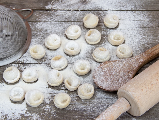 Albóndigas caseras con harina y utensilios de cocina en la mesa de madera rústica. Pelmeni ruso tradicional. Productos semi-terminados.