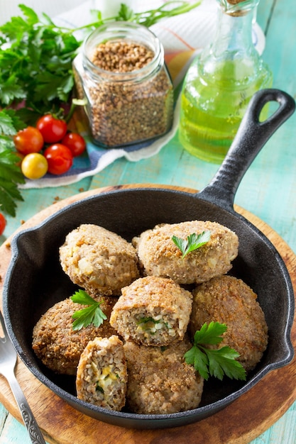 Albóndigas caseras con relleno de trigo sarraceno y huevo Sartén de castiron con deliciosas chuletas fritas hierbas frescas y verduras en la mesa de la cocina