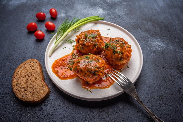 Albóndigas caseras en salsa de tomate en un plato de cerámica blanca con tenedor pan cebollas verdes y