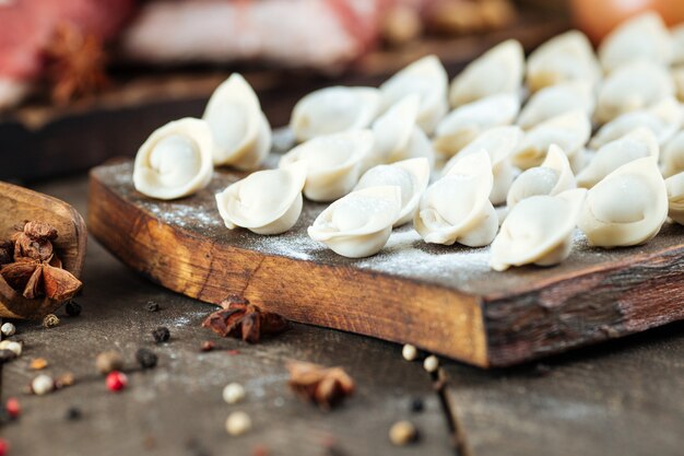 Albóndigas caseras en un tablero con harina en una madera oscura. Plato nacional ruso pelmeni