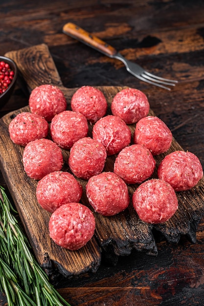 Albóndigas crudas sin cocer de carne molida de res y cerdo con romero. Fondo de madera oscura. Vista superior.