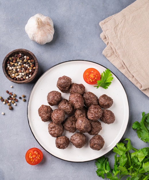 Albóndigas fritas en un plato blanco sobre un fondo azul con hierbas frescas tomates y especias Albóndigas de carne cocinadas en el horno El concepto de alimentación saludable