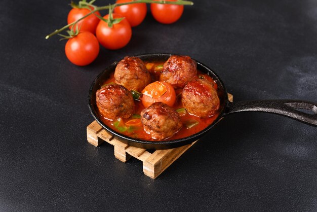 Albóndigas guisadas en salsa de tomate en una sartén sobre un fondo oscuro