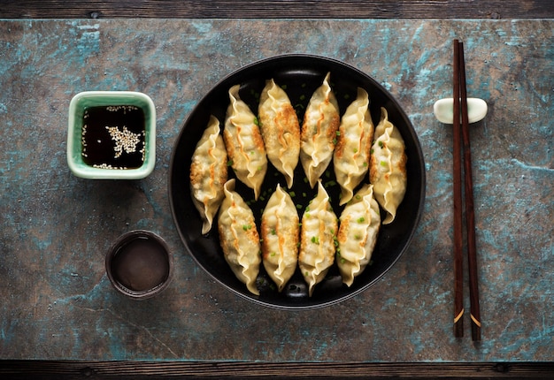 Albóndigas Gyoza fritas en un plato, salsa de soja, palillos y una taza de té verde sobre un fondo de piedra oscura, vista superior