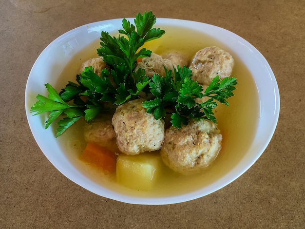 Albóndigas y patatas en sopa de verduras en un plato blanco.