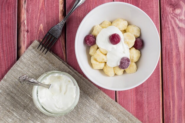 Albóndigas perezosas de requesón ruso, ucraniano tradicional servido con crema agria y cereza sobre fondo de madera