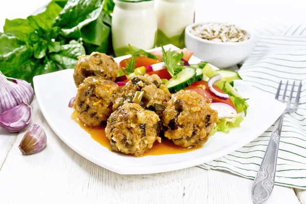 Albóndigas picadas con avena de espinacas y cebollas verdes en salsa de tomate ensalada de verduras en una toalla de plato sobre un fondo de tablero de madera