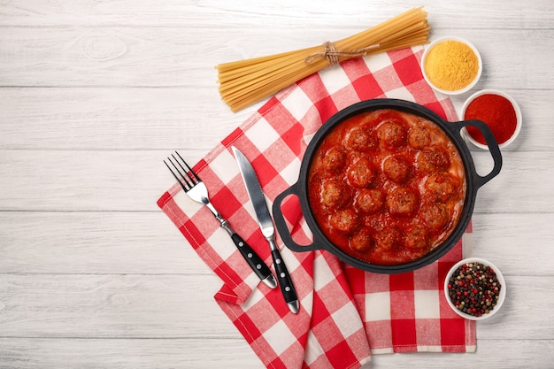 Albóndigas en salsa de tomate con especias en una sartén sobre una tabla de madera blanca