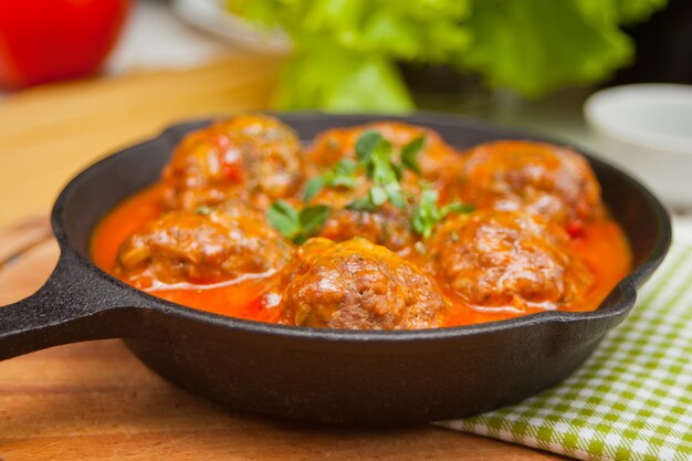 Albóndigas en salsa de tomate picante con hierbas en una sartén de hierro.