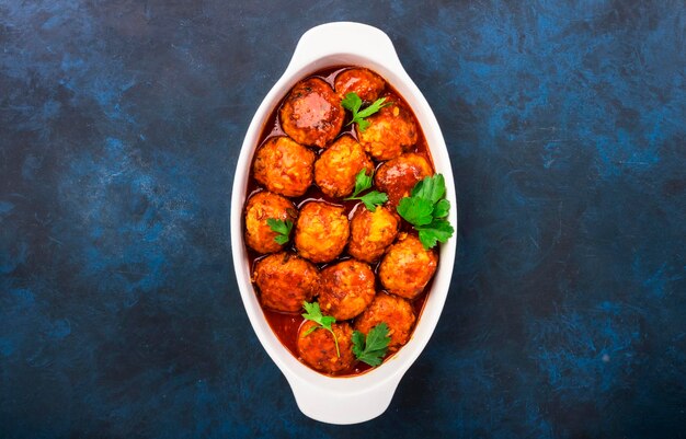 Albóndigas con salsa de tomate picante en un plato blanco para hornear en la mesa de la cocina azul Vista superior