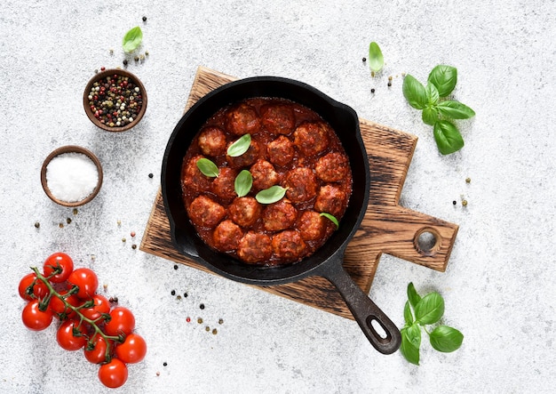 Albóndigas con salsa de tomate en una sartén sobre una superficie de hormigón ligero.