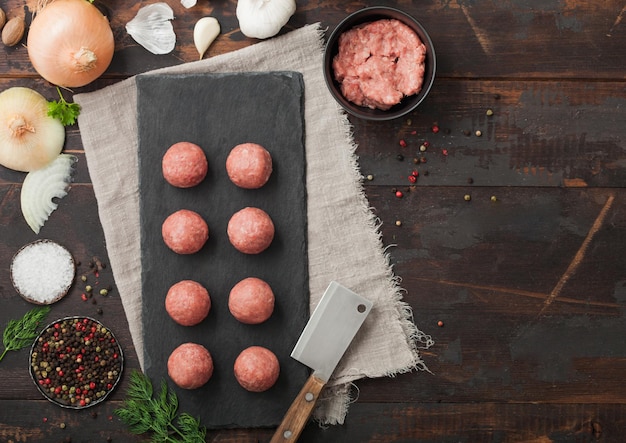 Albóndigas de ternera sobre tabla de piedra con carne picada en un plato con sal de pimienta y ajo sobre fondo oscuro con perejil fresco y cuchilla Espacio para texto