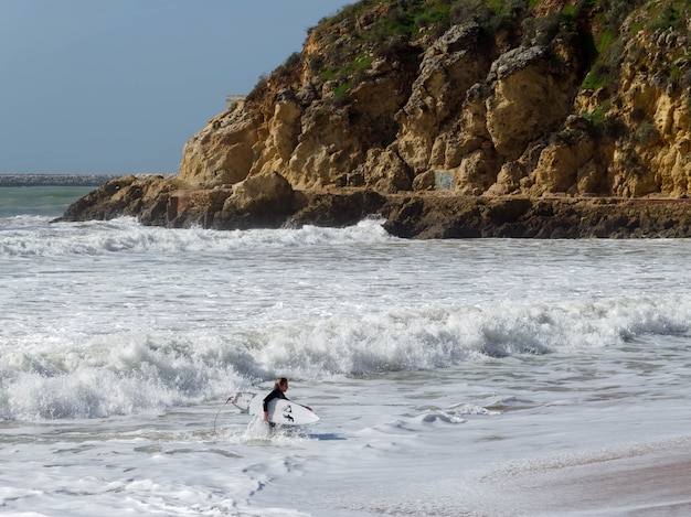 ALBUFEIRA, SÜDALGARVE/PORTUGAL - 10. MÄRZ: Blick auf einen Surfer am Strand von Albufeira in Portugal am 10. März 2018. Nicht identifizierte Person